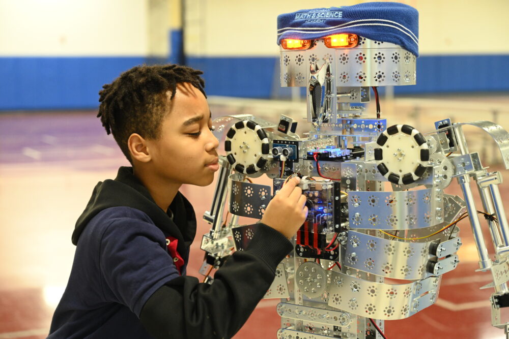 A student at a charter public school focused on adjusting components of a robot, highlighting advanced STEM education and hands-on robotics programs.